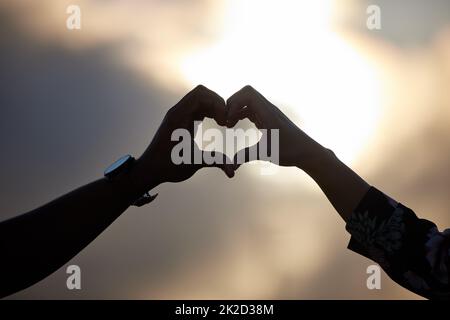 La meilleure chose à retenir dans la vie est l'une l'autre. Photo d'un couple non identifiable faisant une forme de coeur avec leurs mains au coucher du soleil. Banque D'Images