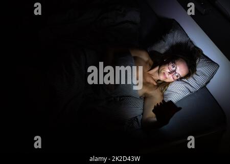 Pretty, middle-aged woman using her tablet ordinateur avant de dormir dans le lit le soir Banque D'Images