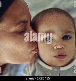 Les mères aiment leurs enfants instinctivement. Photo d'une mère embrassant son adorable bébé garçon sur la joue à la maison. Banque D'Images