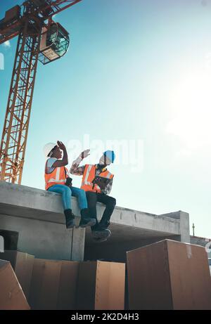 Lorsque votre bureau se sent comme un terrain de jeu. Photo d'un jeune homme et d'une jeune femme assis au-dessus d'un bâtiment sur un chantier de construction et se donnant un haut cinq. Banque D'Images