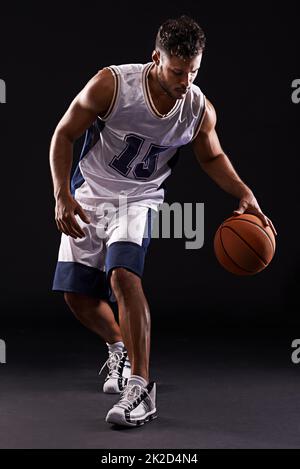 Dribbling pro. Photo studio d'un joueur de basket-ball sur fond noir. Banque D'Images