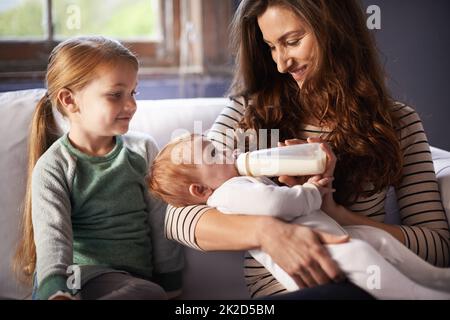 Repas de famille. Prise de vue d'un bébé nourri par sa mère pendant que sa sœur regarde. Banque D'Images