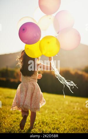 Jolies couleurs au vent. Photo d'une petite fille non identifiable tenant un grand tas de ballons tout en marchant dehors. Banque D'Images