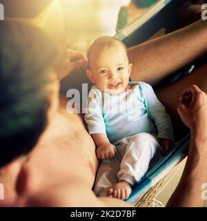 Mon petit homme est si beau. Portrait d'un bébé gai assis sur les genoux de ses pères tout en regardant l'appareil photo dehors à la maison pendant la journée. Banque D'Images