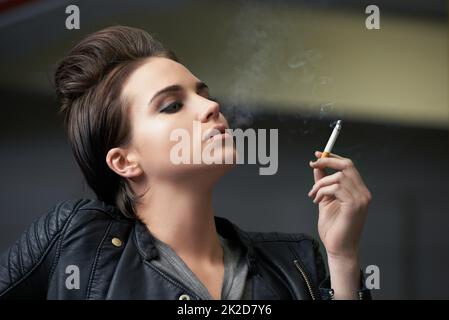 Attitude et attractive. Photo d'une jeune femme rebelle fumant une cigarette dans un garage. Banque D'Images