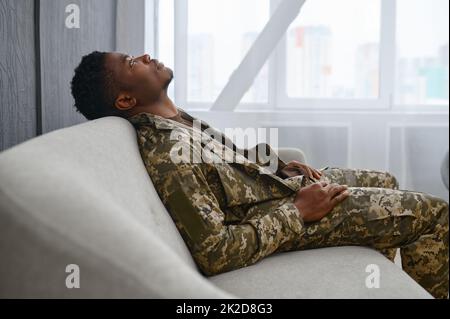 Soldat déprimé en uniforme assis sur le canapé Banque D'Images