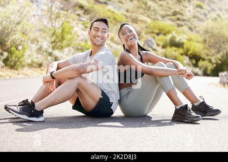 Health, fitness and friends relax after workout in nature, sitting and talking in a road outdoors. Rest, wellness and conversation with diverse man Stock Photo