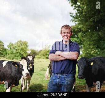 L'agro-industrie est en plein essor. Portrait d'un agriculteur mâle debout avec ses bras plié sur sa ferme laitière. Banque D'Images