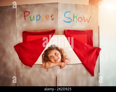 Encourager l'imagination des enfants par le jeu. Photo d'une adorable petite fille debout dans la fenêtre d'un théâtre de marionnettes à la maison. Banque D'Images