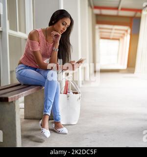 Il semble que la classe soit annulée aujourd'hui. Prise de vue d'une jeune femme attirante utilisant son téléphone portable tout en étant assise sur un banc. Banque D'Images