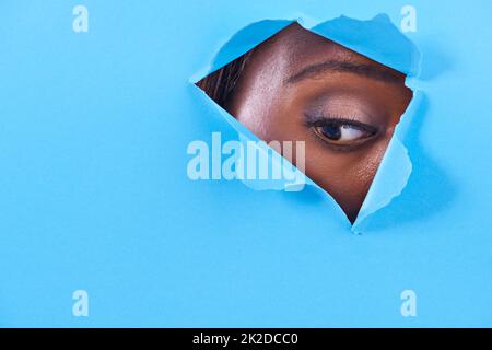 Whats that down there. A view of a womans eye looking through a hole in some colorful paper. Stock Photo