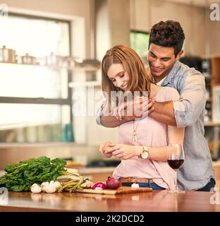 La nourriture est amour pour votre estomac. Photo d'un jeune homme qui embrasse sa femme pendant qu'elle prépare le dîner. Banque D'Images