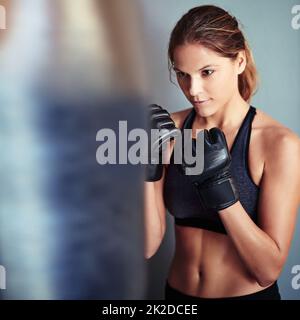 La puissance provient d'une bonne technique. Photo d'un boxeur féminin qui s'occupe d'un sac de poinçonnage. Banque D'Images