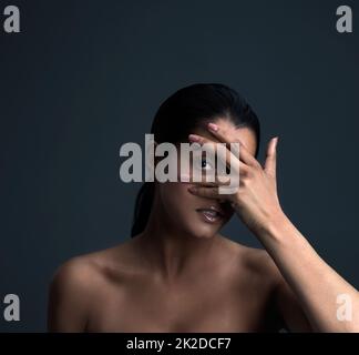 La beauté est dans l'œil du porte-bec. Photo studio d'une belle jeune femme posant sur un arrière-plan sombre. Banque D'Images