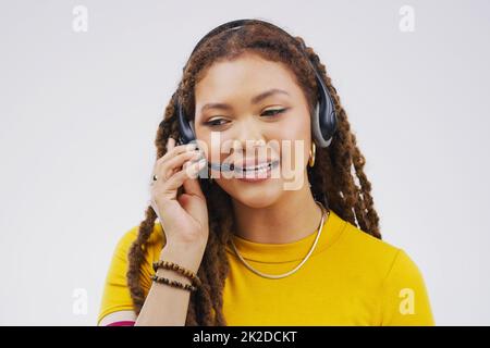 Service avec le sourire. Photo en studio d'une jeune représentante attirante du service clientèle portant un casque sur fond gris. Banque D'Images