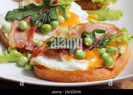 Bruschetta avec rucola, chrispy bacon, petits pois et œuf poché servi sur plaque blanche Banque D'Images