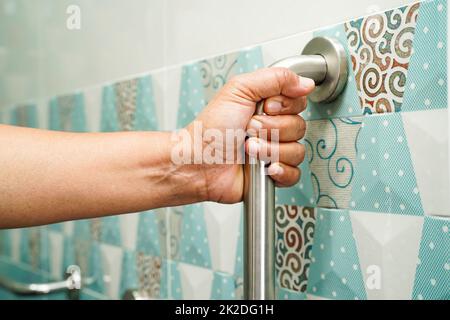 Asian woman patient use toilet support rail in bathroom, handrail safety grab bar, security in nursing hospital. Stock Photo