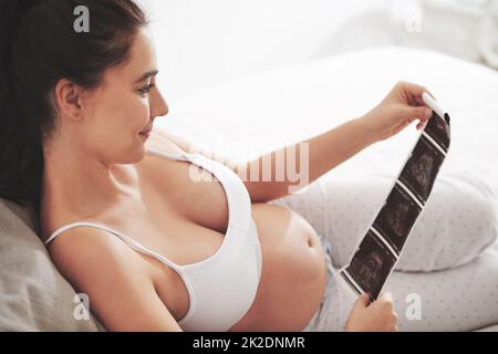 L'amour à première vue. Prise de vue d'une femme enceinte regardant une image d'un échogramme à la maison. Banque D'Images