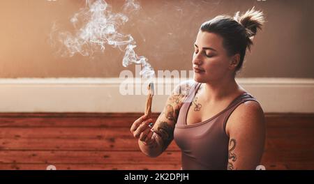 Il permet d'améliorer la clarté et la concentration. Photo d'une jeune femme brûlant un bâton de palo santo à la maison. Banque D'Images