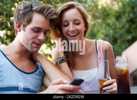 Socialiser au XXIe siècle. Un adorable couple d'adolescents partageant un MP3 joueurs et écoutant de la musique tout en appréciant leurs boissons. Banque D'Images