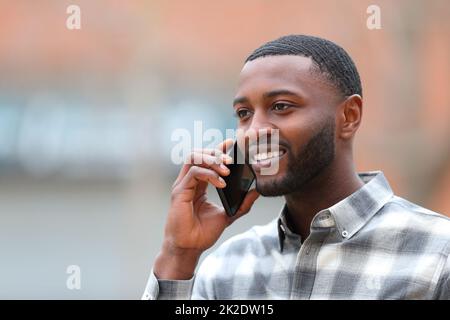 Un homme heureux avec une peau noire parlant sur un téléphone portable dans la rue Banque D'Images