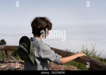 Un adolescent se tient sur une terrasse d'observation en hauteur dans les montagnes et regarde au loin. Banque D'Images