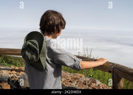 Un adolescent se tient sur une terrasse d'observation en hauteur dans les montagnes et regarde au loin. Banque D'Images
