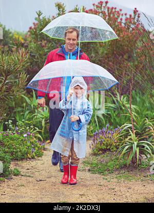 Marche sous la pluie. Photo en longueur d'un père et de son fils marchant dehors sous la pluie. Banque D'Images