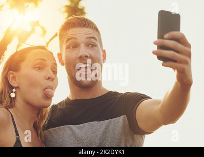 Mettre sur leurs visages de selfie stupides. Photo d'un jeune couple stupide posant pour un selfie ensemble à l'extérieur. Banque D'Images