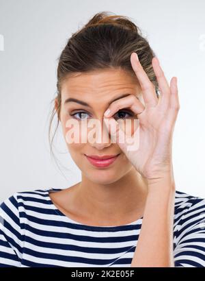 Prêt pour le bal masqué. Photo d'une belle jeune femme utilisant ses doigts pour faire un anneau autour de son œil. Banque D'Images