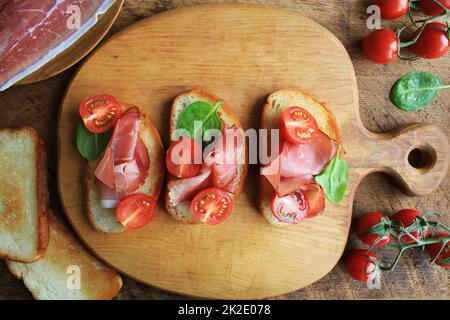 Bruschetta avec jambon prosciutto, tomates cerises et épinards verts sur planche à découper. Vue de dessus Banque D'Images