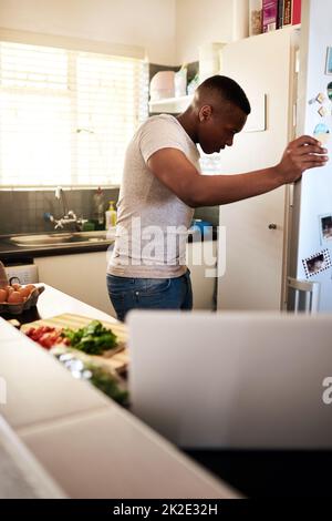 J'ai l'impression de manquer quelque chose Petit plan d'un jeune homme beau regardant dans son réfrigérateur tout en faisant le petit déjeuner dans sa cuisine à la maison. Banque D'Images