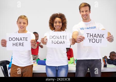 Aidez dès aujourd'hui. Portrait de bénévoles tenant des affiches tout en travaillant avec de petits enfants. Banque D'Images