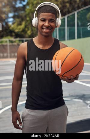 Nous vous aimais à tirer un peu de cerceau. Portrait d'un jeune sportif qui écoute de la musique tout en jouant au basket-ball sur un terrain de sport. Banque D'Images