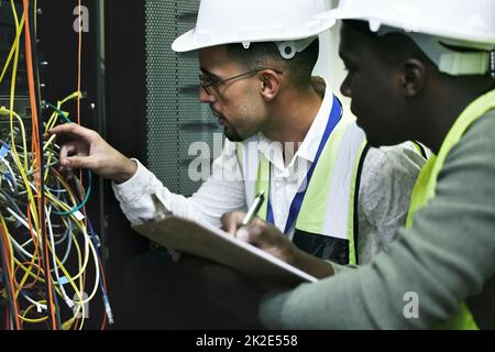 C'est ce qu'ils font pour détourner les problèmes technologiques. Photo de deux techniciens travaillant ensemble dans une salle de serveur. Banque D'Images