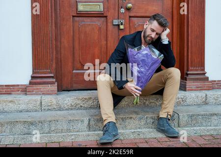 Compte tenu de l'épaule froide. Photo d'un beau jeune homme à l'air déprimé en attendant avec un bouquet de fleurs sur une marche. Banque D'Images