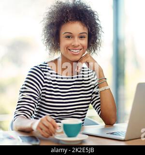 Le travail indépendant est la voie à suivre. Portrait d'une jeune femme buvant un café tout en travaillant sur un ordinateur portable à la maison. Banque D'Images