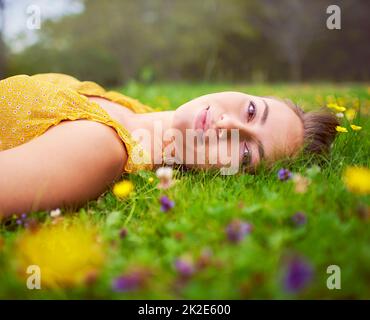 J'ai trouvé mon bonheur dans un champ plein de fleurs. Portrait d'une jeune femme couché dans un champ d'herbe et de fleurs. Banque D'Images