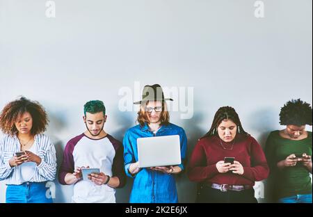 Utilisé avec le support. Photo en studio d'un groupe de jeunes debout contre un mur et utilisant la technologie sans fil. Banque D'Images