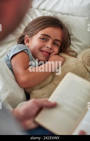 Ont-ils fini heureux après. Coupe courte d'une petite fille couchée au lit pendant que son père lui lit une histoire. Banque D'Images