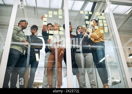 En travaillant à travers leurs meilleurs concepts. Photo d'un groupe de personnes en voyage d'affaires avec des notes sur un mur de verre dans un bureau. Banque D'Images