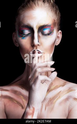 Perdu dans un révérence coloré. Photo studio d'une jeune femme posant avec de la peinture sur son visage isolé sur le noir. Banque D'Images