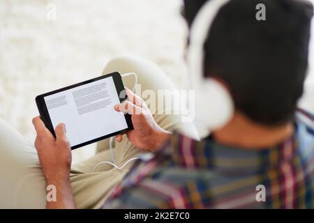 La musique est source d'inspiration. Photo d'un jeune homme qui écoute de la musique sur sa tablette tout en se relaxant sur le canapé à la maison. Banque D'Images