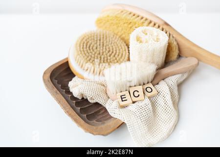 Zéro déchet, salle de bain durable et style de vie. Pinceau de bambou, éponge de loofah, pinceau de massage de cactus sur fond blanc. L'inscription Eko en lettres de bois. Banque D'Images