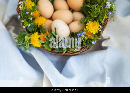 Beau bouquet de printemps dans un panier en bois où se trouvent les oeufs peints de Pâques, un oeuf avec un visage mignon. Banque D'Images