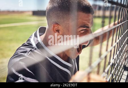 Si vous n'êtes pas passionné, vous n'êtes pas fan. Prise de vue d'un jeune homme regardant une partie de baseball depuis l'arrière de la clôture. Banque D'Images