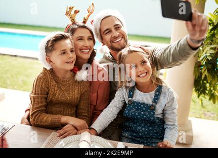 Étaient toujours prêts pour un selfie de Noël. Prise de vue rognée d'une famille de quatre personnes prenant un selfie ensemble le jour de Noël. Banque D'Images