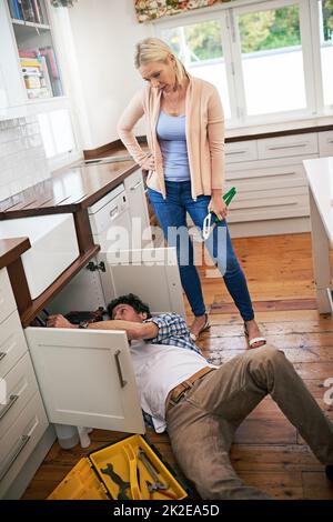 Miel, je pense que nous devrions juste appeler un professionnel. Photo d'un homme fixant des tuyaux sous son évier de cuisine pendant que sa femme regarde. Banque D'Images