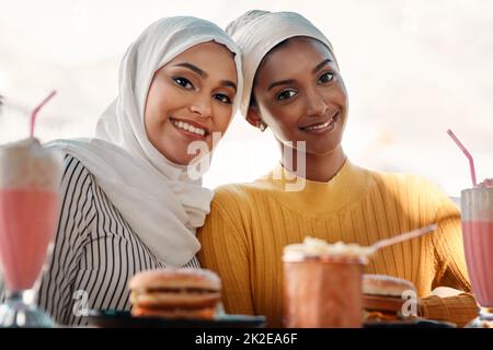 C'est là que vous nous trouverez le week-end. Portrait court de deux jeunes amies affectueuses ayant un repas ensemble dans un café tout en étant vêtues de hijab. Banque D'Images