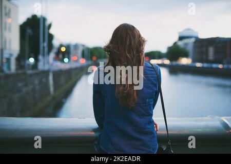 Découvrez les sites touristiques. Vue arrière d'une jeune femme méconnue qui a vue sur la ville en se tenant sur un pont. Banque D'Images